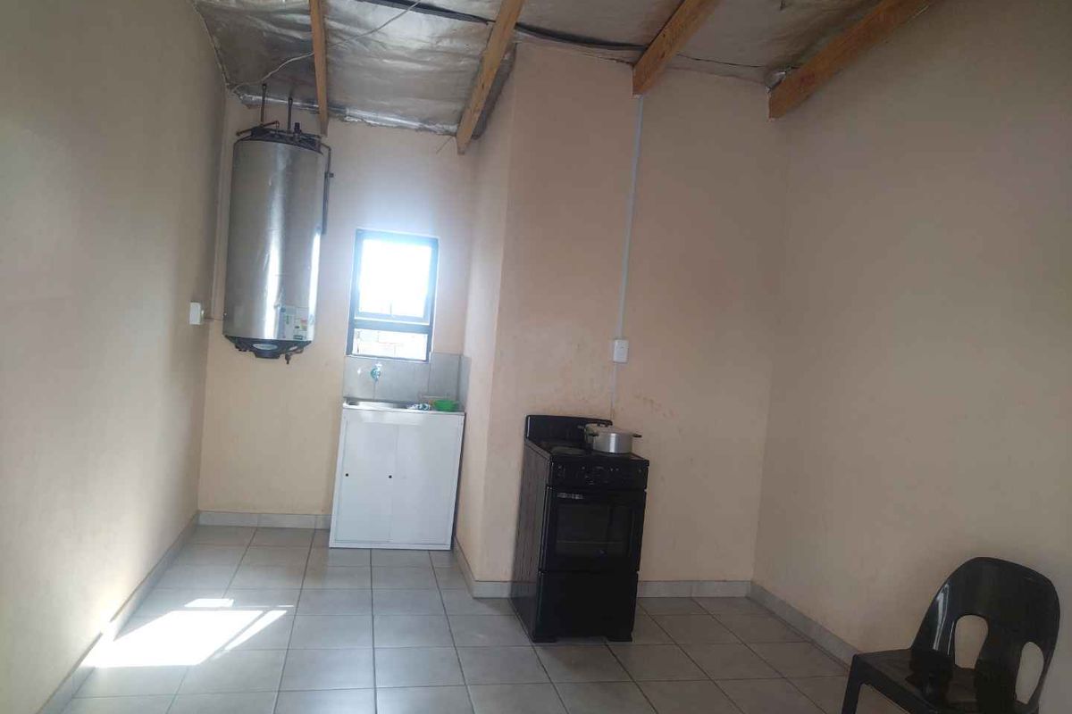 A basic kitchen area featuring tiled flooring, a small sink unit, and a freestanding stove, with an exposed ceiling structure.