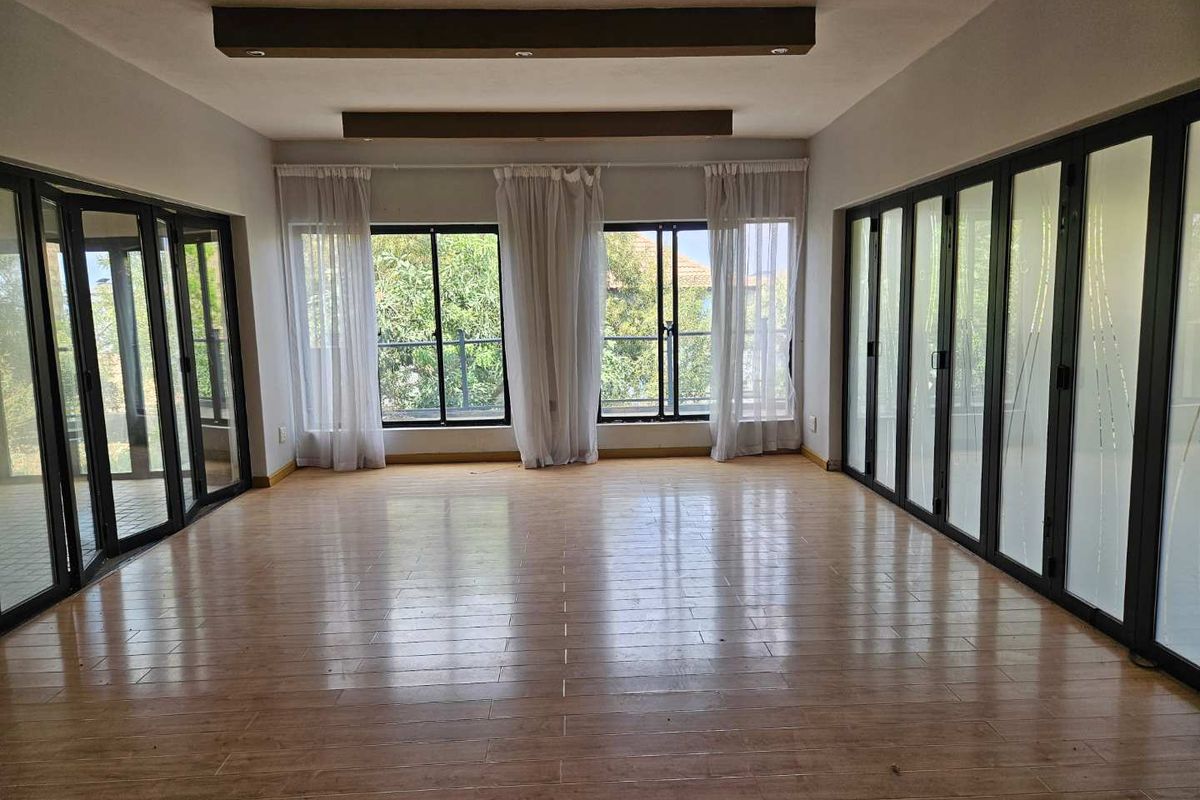 Spacious living area featuring wood-look tile flooring, recessed ceiling beams, and extensive bi-fold glass doors providing abundant natural light and outdoor access.