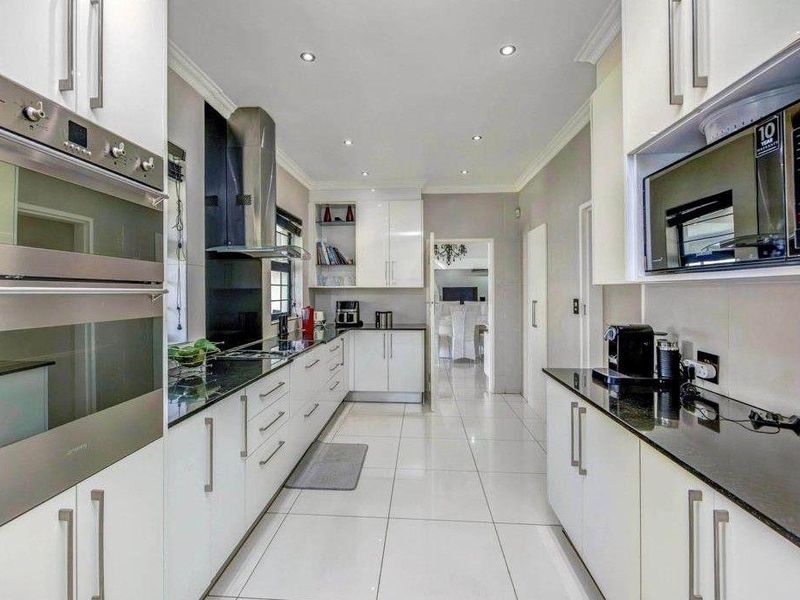 Modern galley-style kitchen featuring white cabinetry, sleek granite countertops, integrated stainless steel appliances, and polished floor tiles with recessed ceiling lighting.