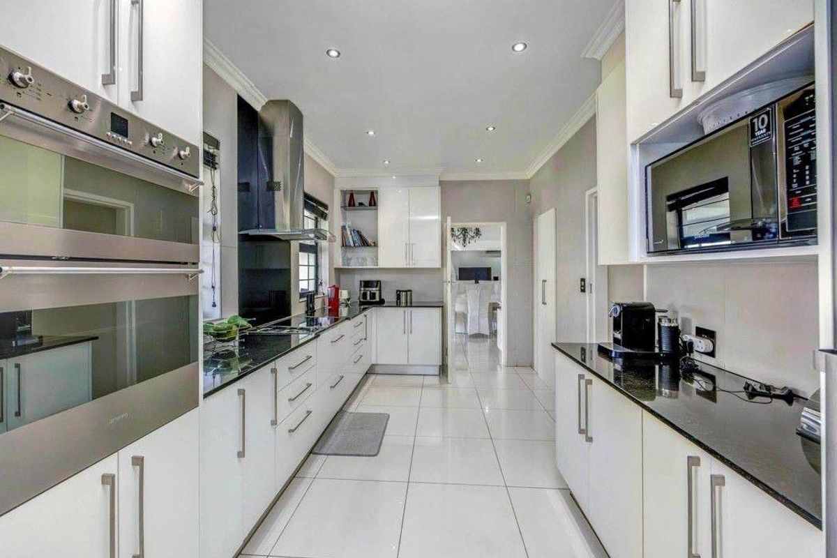 Modern galley-style kitchen featuring white cabinetry, sleek granite countertops, integrated stainless steel appliances, and polished floor tiles with recessed ceiling lighting.