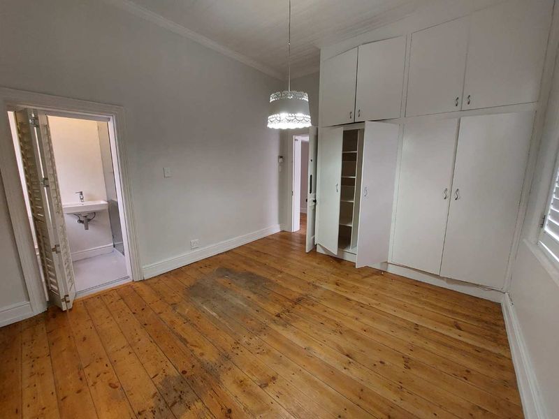 A spacious bedroom featuring original timber flooring, extensive built-in cupboard storage, and direct access to an en-suite bathroom.