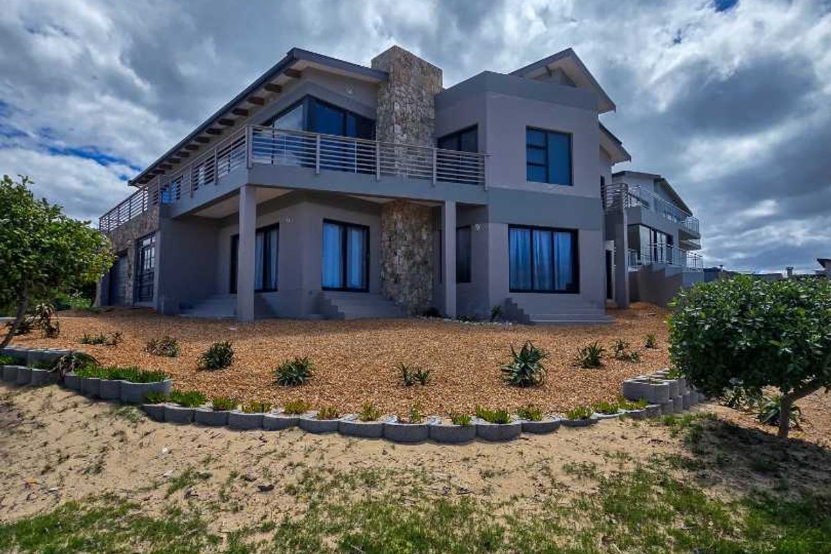 A modern multi-story residential property featuring stone cladding, expansive balconies, and a landscaped garden area with gravel beds.