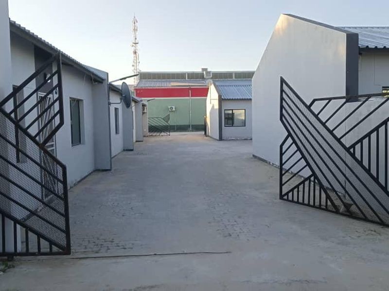 A view of the business property entrance featuring a concrete driveway and metal security gates leading to the building complex.