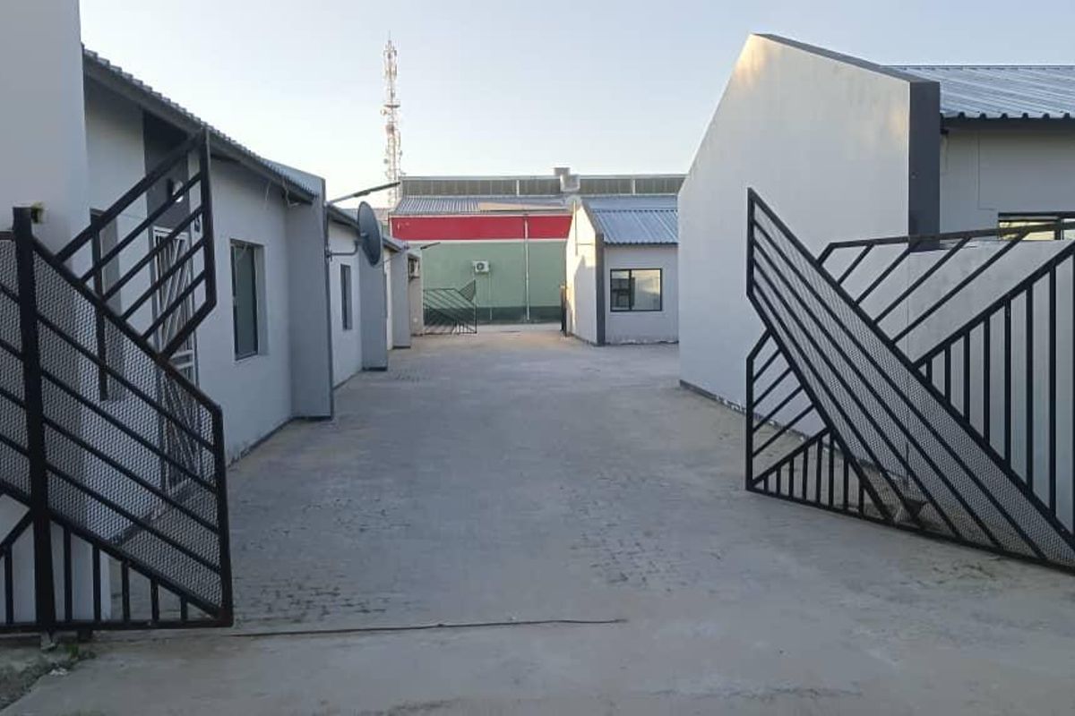 A view of the business property entrance featuring a concrete driveway and metal security gates leading to the building complex.
