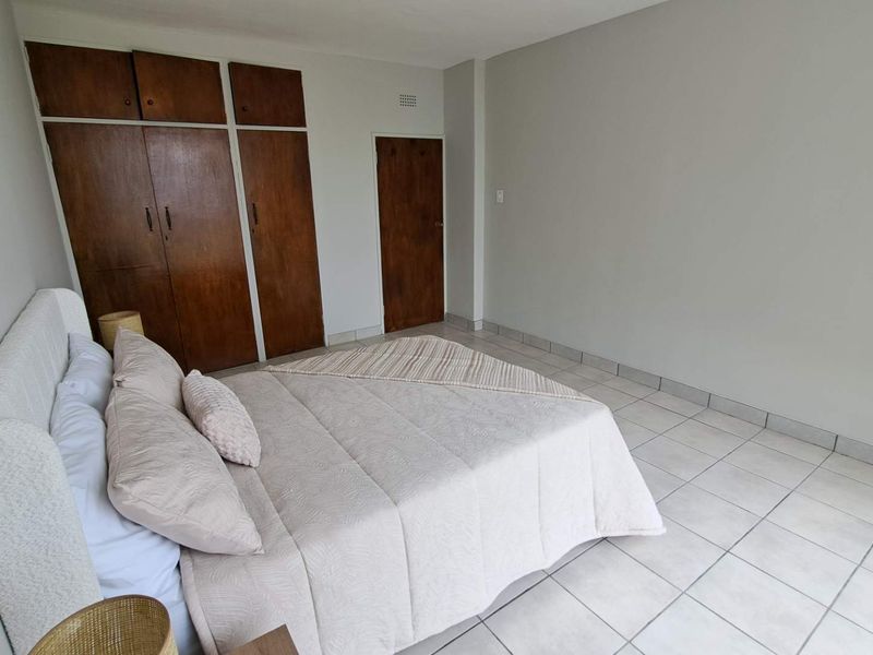 A bedroom featuring tiled flooring and built-in wooden cupboards, offering a functional space with neutral wall finishes.