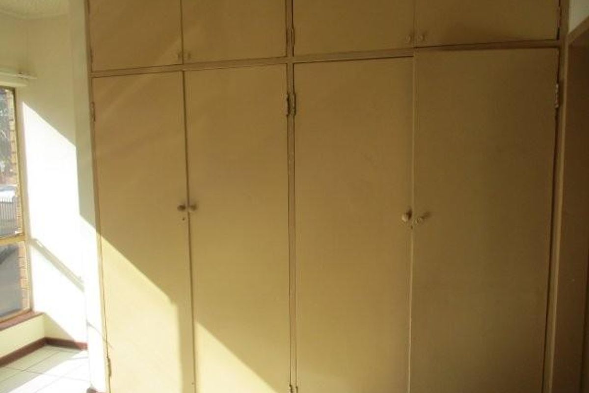 A bedroom featuring floor-to-ceiling built-in cupboards with a dated finish and tiled flooring.