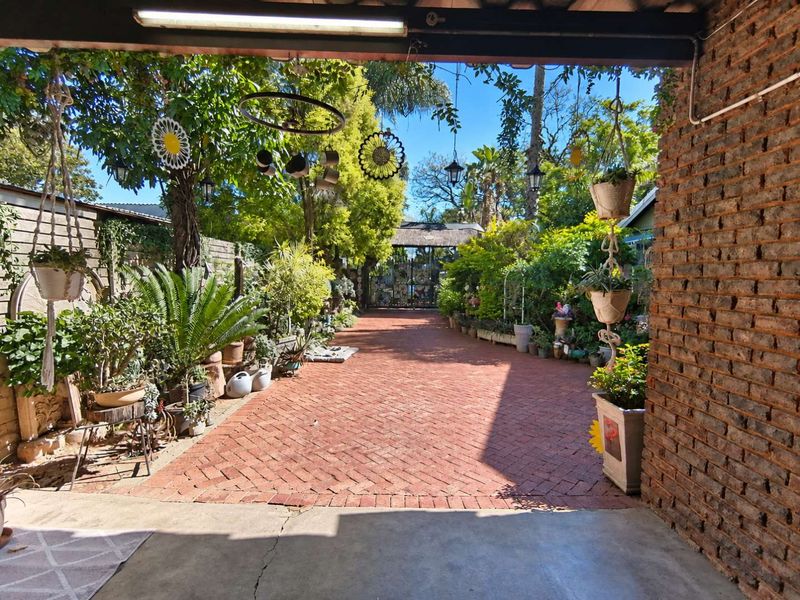 A covered patio area featuring brick paving and an exposed brick wall, leading out into a lush, landscaped garden space.