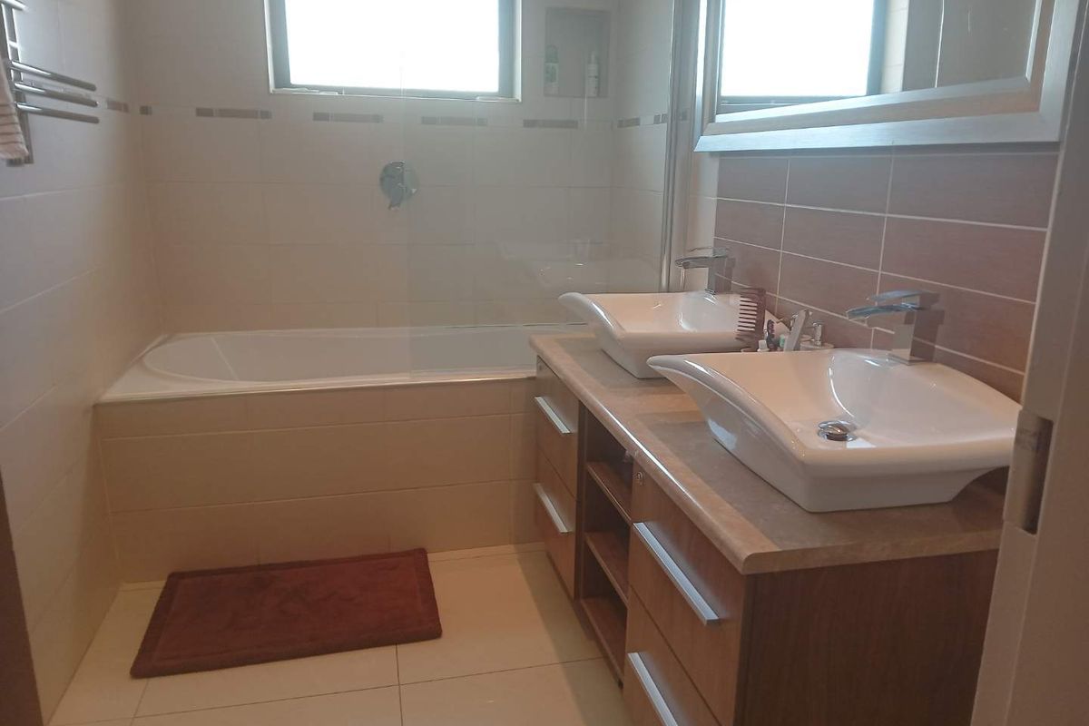 A modern bathroom featuring a double vanity with vessel sinks, a built-in bathtub with a glass screen, and neutral wall tiling.