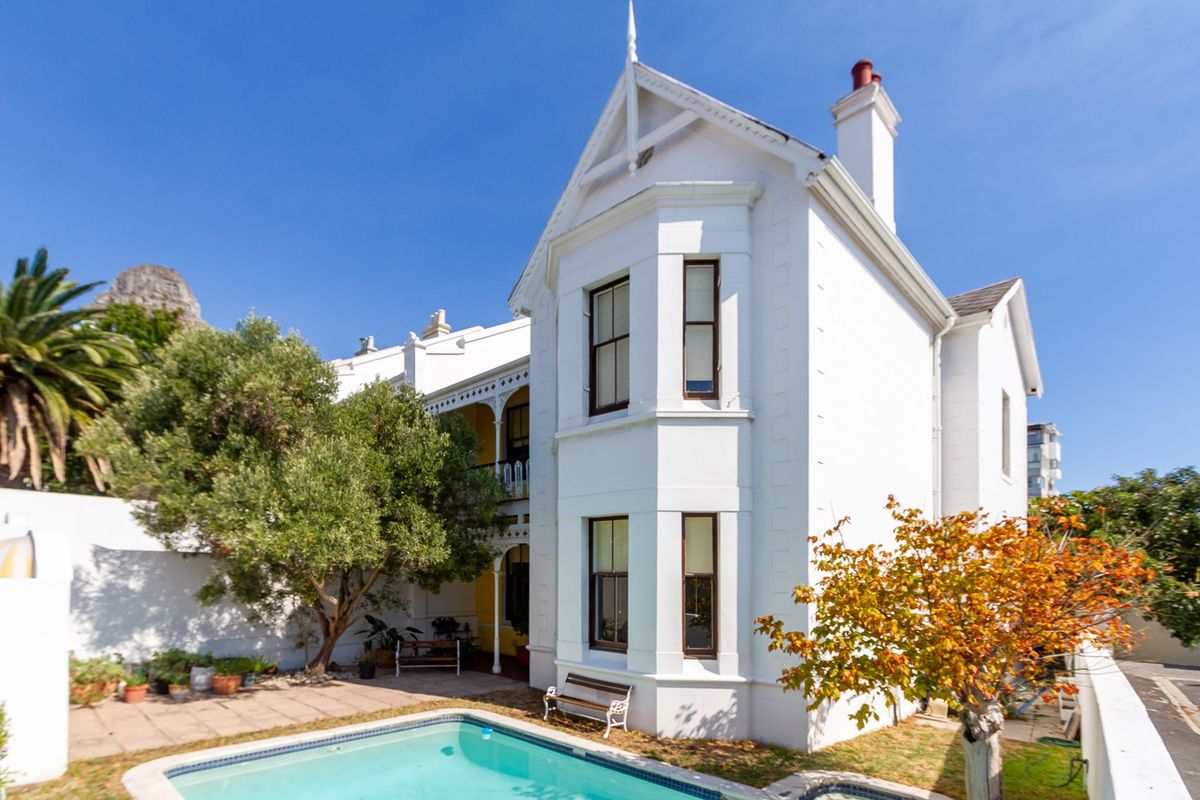 A well-maintained historic house exterior featuring a white facade, a swimming pool, and a paved patio area with established garden trees.