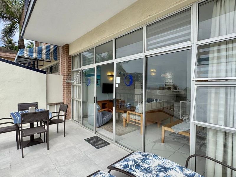 A covered balcony featuring tiled flooring, aluminium sliding doors, and a brick wall, providing a seamless transition to the interior living space.