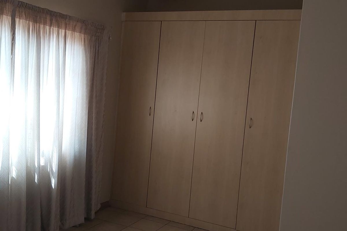 A bedroom featuring built-in wooden cupboards and tiled flooring, offering a neutral space with natural light from the window.