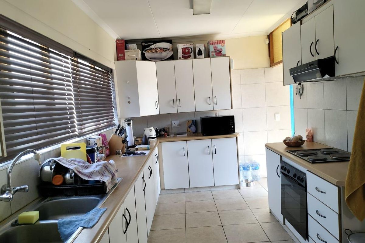 Functional kitchen featuring white cabinetry, laminate countertops, built-in oven, electric hob, and double stainless steel sink with tiled splashbacks.