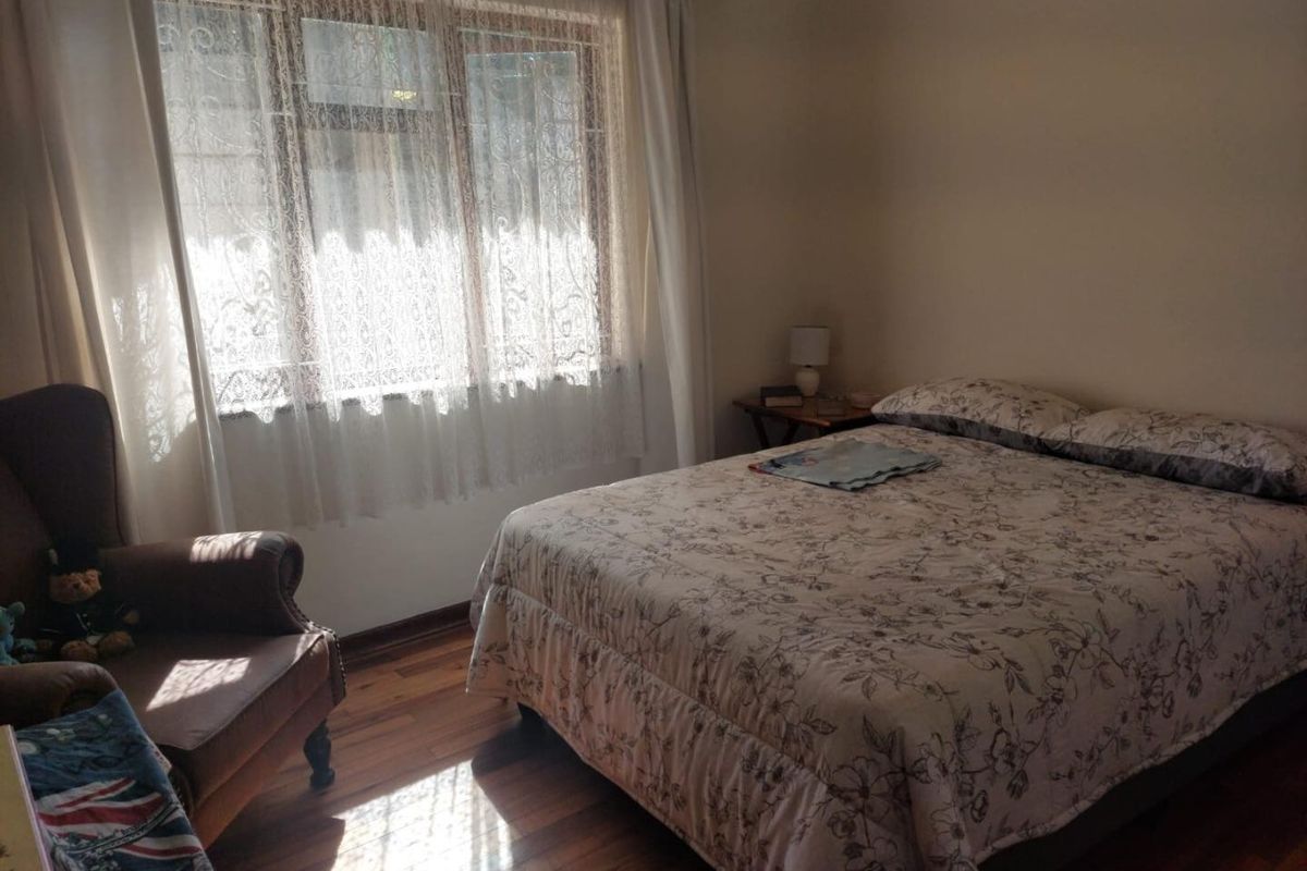 A bedroom featuring hardwood flooring and a large window with natural light.