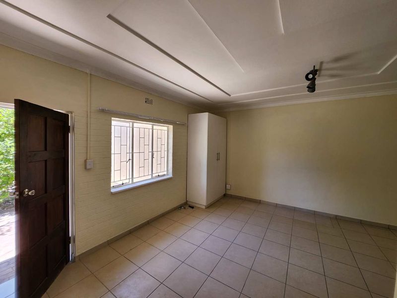 A bright, empty bedroom featuring tiled flooring, a built-in wardrobe, and a window with security bars, offering a clean canvas for personalization.