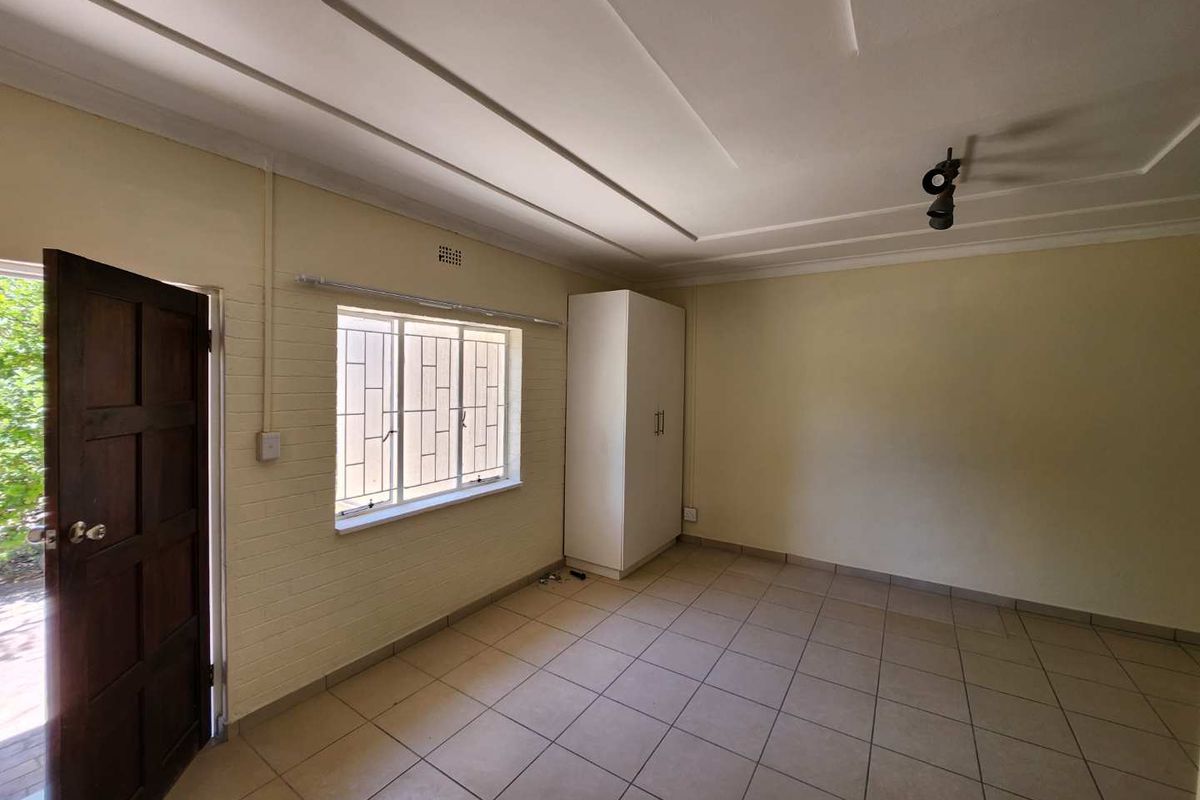 A bright, empty bedroom featuring tiled flooring, a built-in wardrobe, and a window with security bars, offering a clean canvas for personalization.