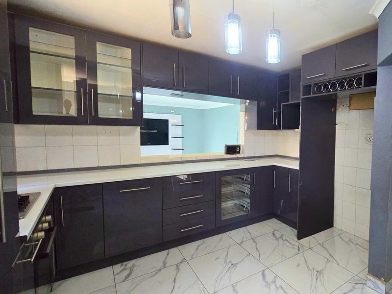 Modern kitchen featuring dark high-gloss cabinetry, white stone countertops, marble-effect floor tiles, and integrated appliances, offering a sleek and contemporary culinary space.