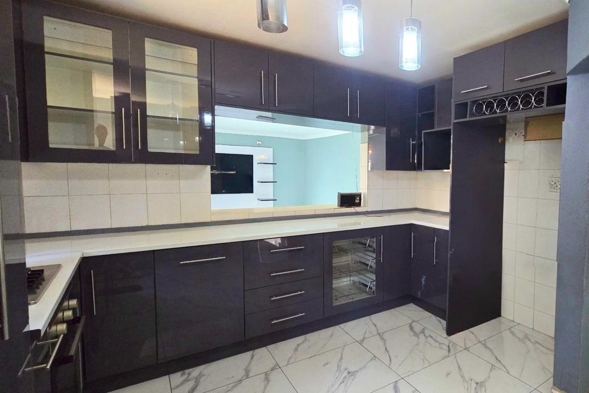 Modern kitchen featuring dark high-gloss cabinetry, white stone countertops, marble-effect floor tiles, and integrated appliances, offering a sleek and contemporary culinary space.