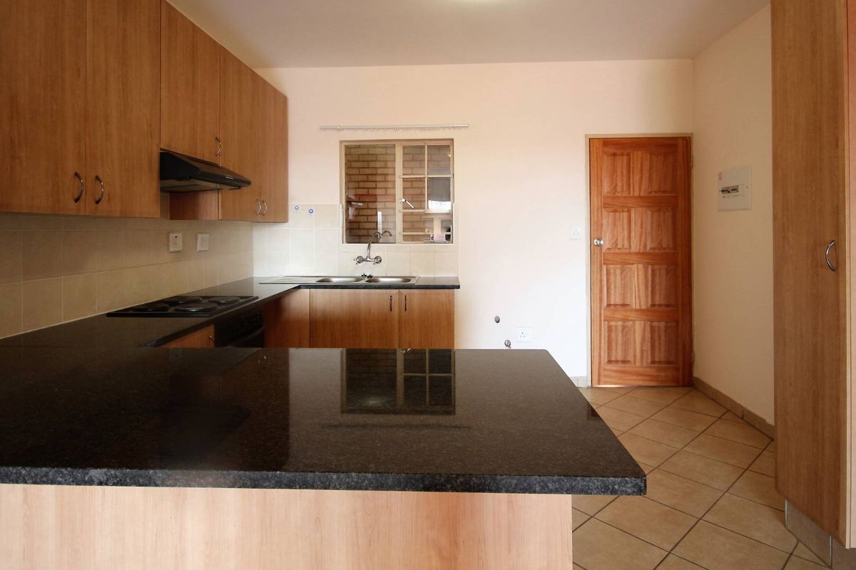 A clean, functional kitchen featuring laminate cabinetry, granite countertops, an electric hob with extractor fan, and tiled flooring.