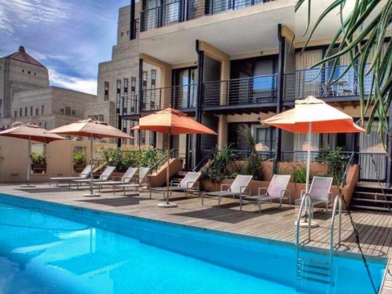 A communal swimming pool area featuring timber decking and direct access to the apartment building's lower level balconies.