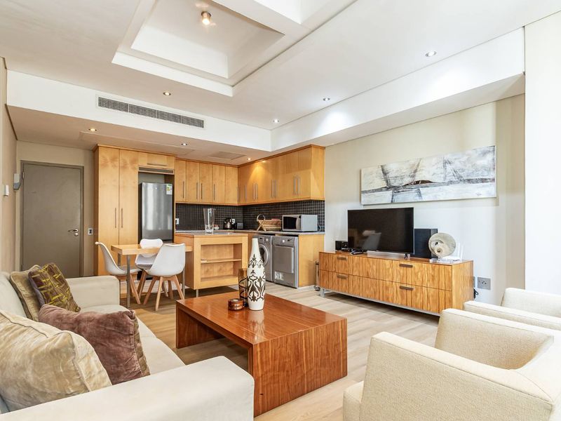 Modern open-plan living area featuring a well-appointed kitchen with built-in cabinetry, recessed lighting, and ducted air conditioning in a contemporary apartment setting.