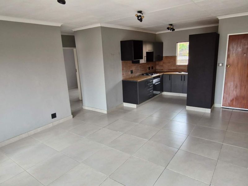 An open-plan living and kitchen area featuring modern dark cabinetry, built-in appliances, and neutral tiled flooring throughout.