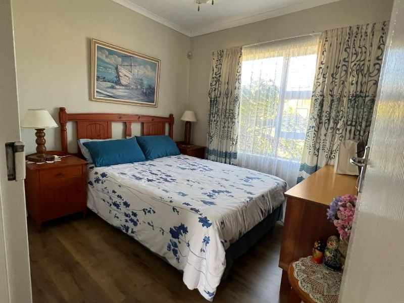 A well-maintained bedroom featuring laminate flooring, a ceiling fan, and natural light through a large window.