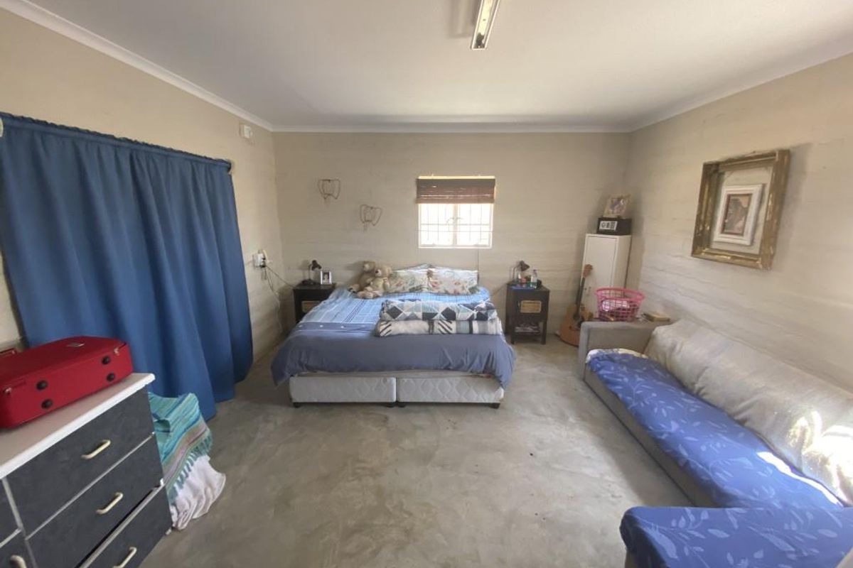 A spacious bedroom featuring exposed wall finishes, concrete flooring, and a functional layout with natural light from a central window.