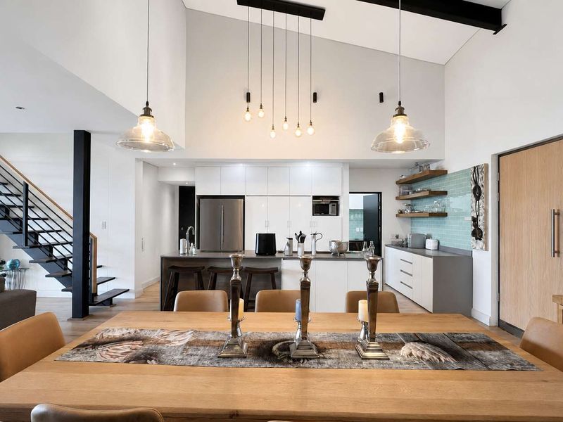 Spacious open-plan living and dining area featuring a modern kitchen with island, vaulted ceilings, and a striking staircase.