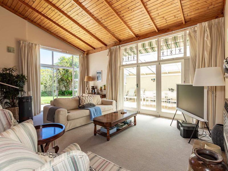 Spacious living room featuring a high exposed timber ceiling, large glass doors providing natural light, and direct access to the outdoor patio and garden.