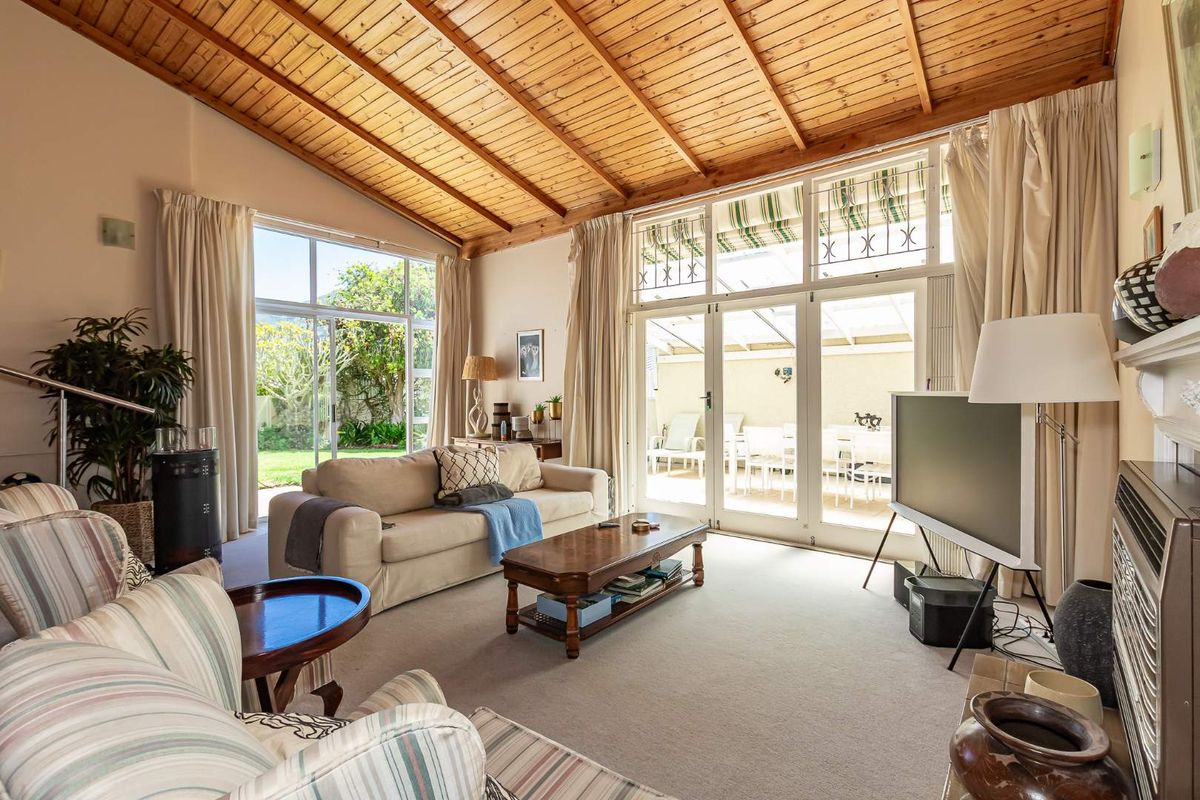 Spacious living room featuring a high exposed timber ceiling, large glass doors providing natural light, and direct access to the outdoor patio and garden.