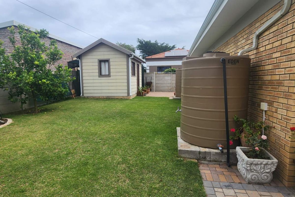A well-maintained rear garden featuring a lawn, a detached outbuilding, and a large water storage tank installed against the brick exterior wall.