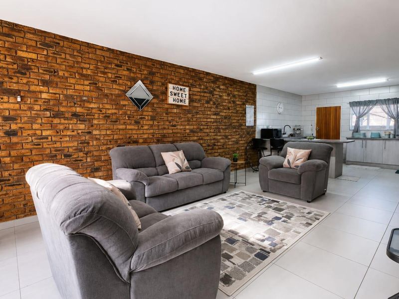 Open-plan living area featuring an exposed brick wall, tiled flooring, and an integrated kitchen space with functional cabinetry and sink.