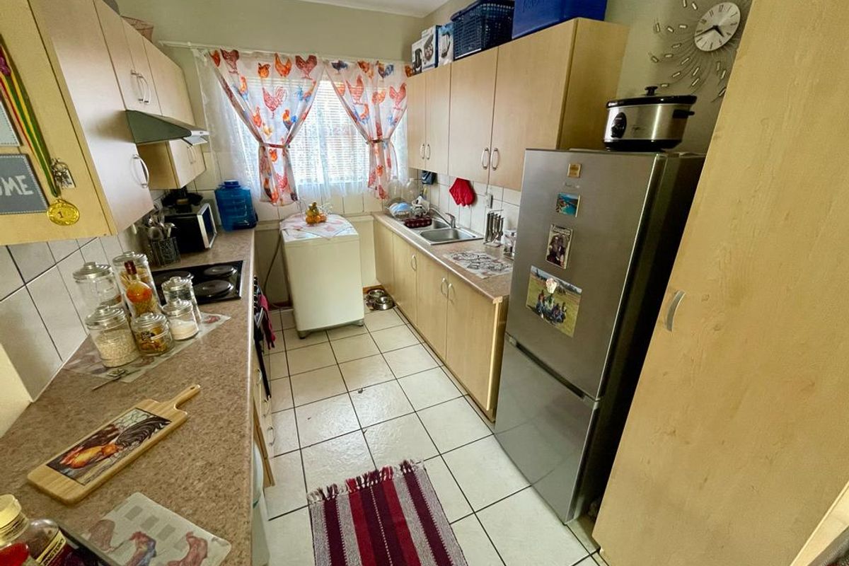 A functional galley-style kitchen featuring light wood-finish cabinetry, laminate countertops, tiled flooring, and integrated sink and cooktop fixtures.