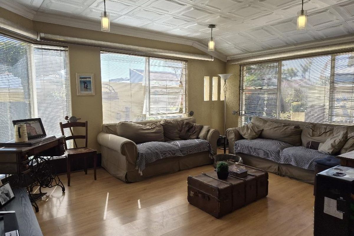 Spacious living room featuring laminate flooring, a decorative coffered ceiling, and large windows that provide ample natural light.