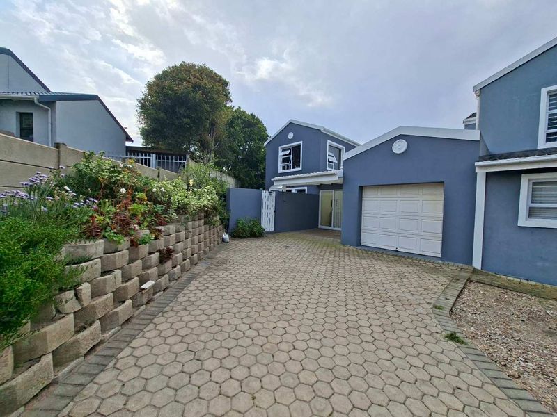 Front exterior view of the property featuring a paved driveway, garage, and a landscaped retaining wall along the boundary.