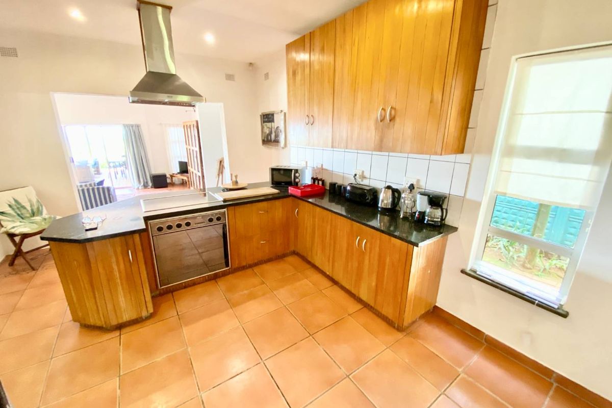 A functional kitchen featuring wooden cabinetry, granite countertops, stainless steel appliances, and tiled flooring, with an open-plan layout leading to the living area.