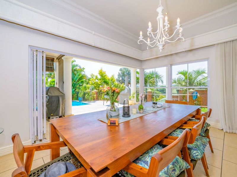Bright dining room featuring elegant chandelier lighting, tiled floors, and expansive folding doors that open directly to the outdoor patio and pool area.