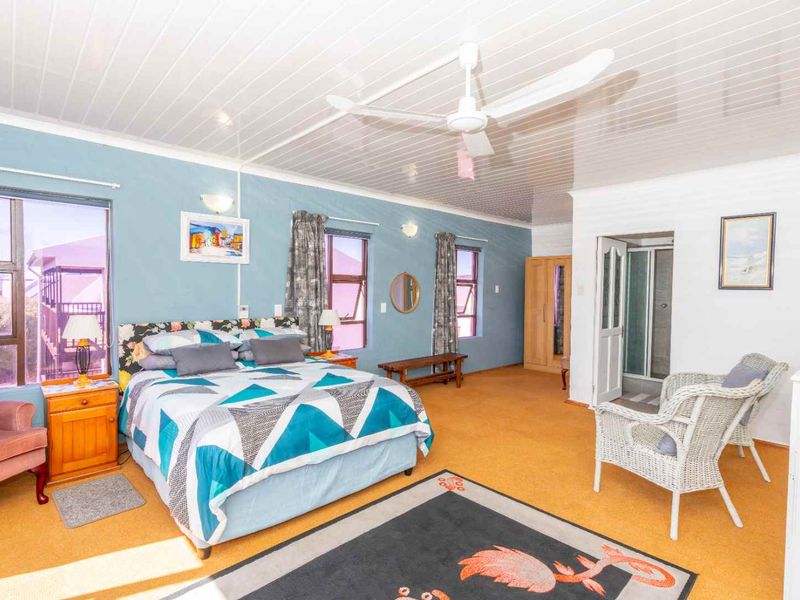 Spacious bedroom featuring a ceiling fan, en-suite bathroom access, and large windows providing natural light.