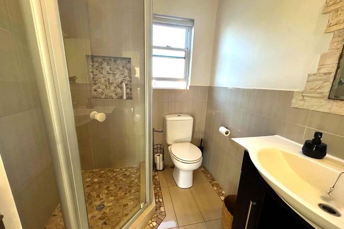 A functional bathroom featuring a glass-enclosed shower with mosaic tile accents, a standard toilet, and a modern vanity unit.