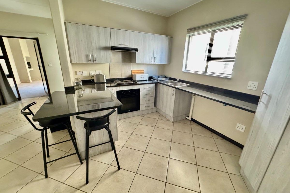 Modern kitchen featuring light wood-grain cabinetry, dark granite countertops, a built-in oven, hob, extractor fan, and a breakfast bar island.
