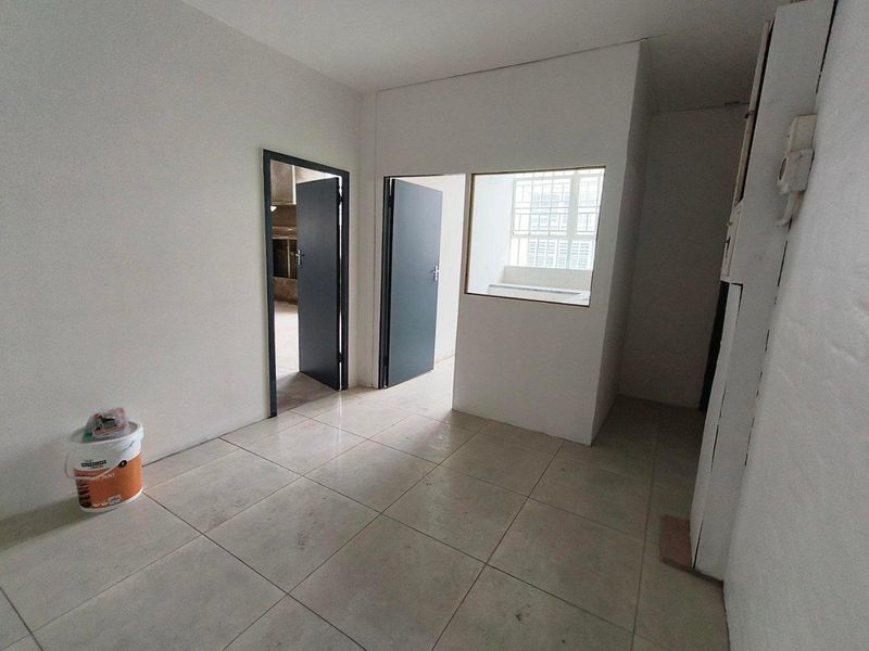A vacant hallway area featuring neutral tiled flooring, internal doors, and a small internal window, presenting a clean slate for industrial or office use.