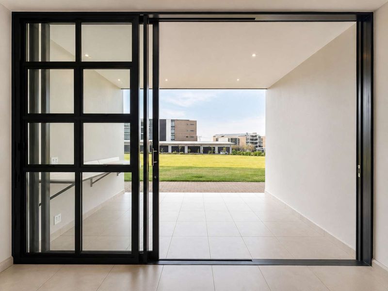 A modern, covered patio featuring large sliding glass doors, neutral tiled flooring, and recessed lighting, overlooking a landscaped communal garden area.
