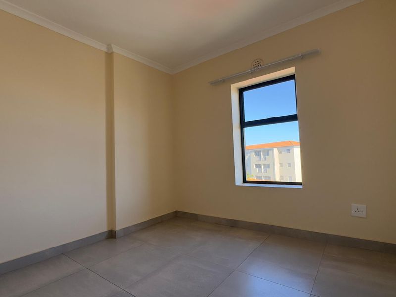 A clean, empty bedroom featuring neutral wall paint, large format floor tiles, and a window with a black frame.