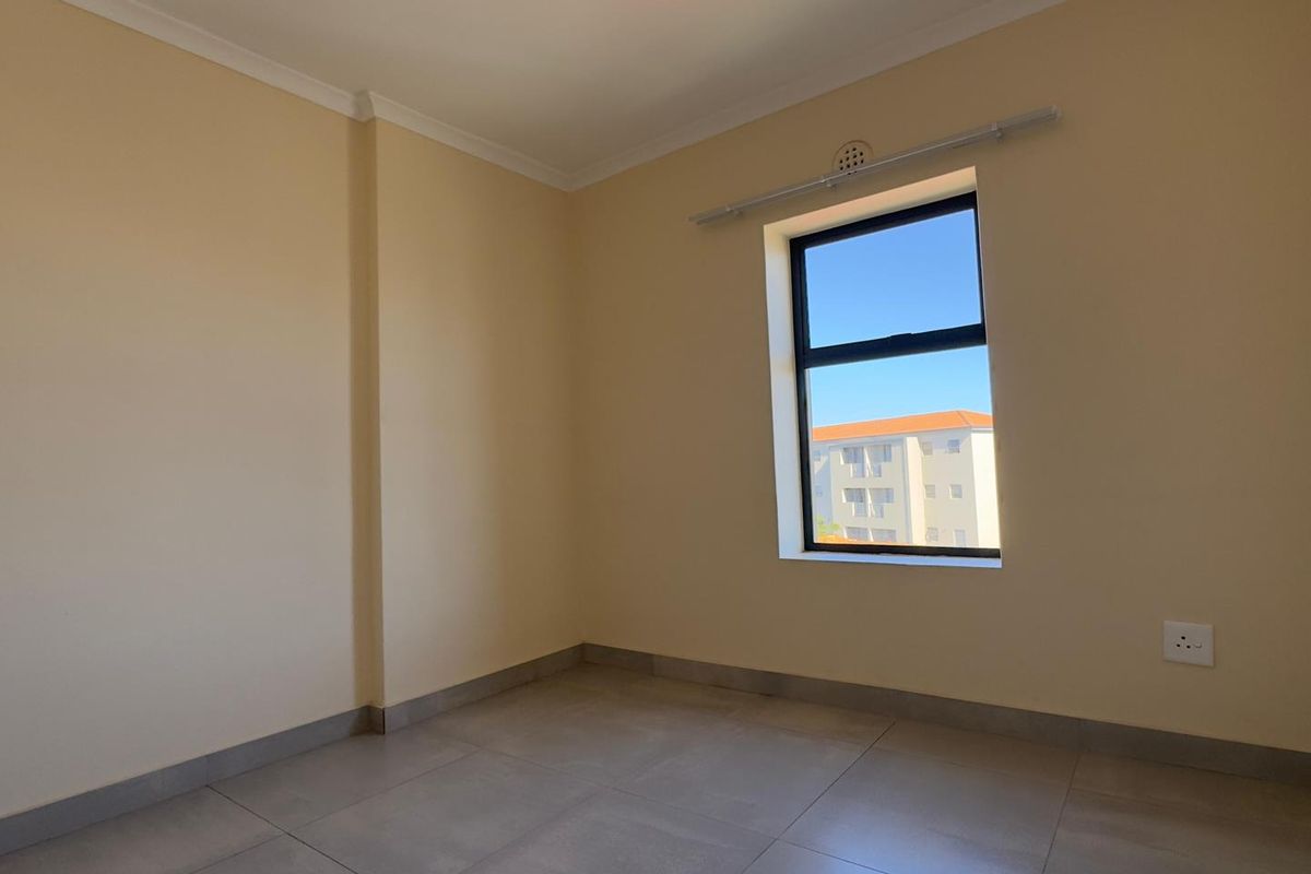 A clean, empty bedroom featuring neutral wall paint, large format floor tiles, and a window with a black frame.
