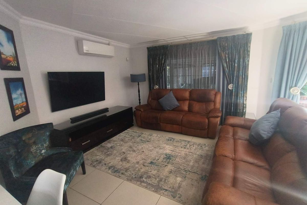 A comfortable living room featuring large floor tiles, a wall-mounted air conditioning unit, and expansive windows with curtains.