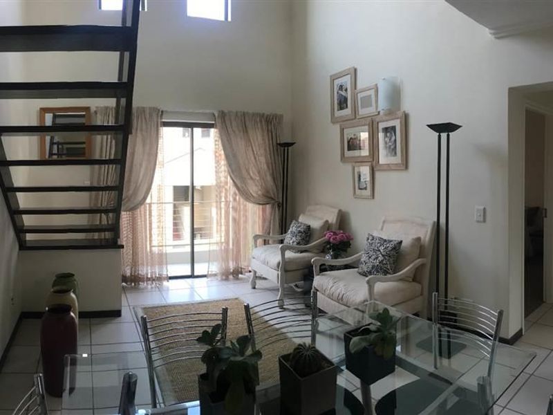 Open plan living area featuring a double volume ceiling, tiled flooring, and a modern staircase leading to the upper level.