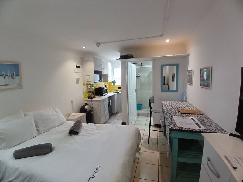 An open-plan studio apartment featuring a compact kitchen area, tiled flooring throughout, and an adjoining bathroom with a shower enclosure.
