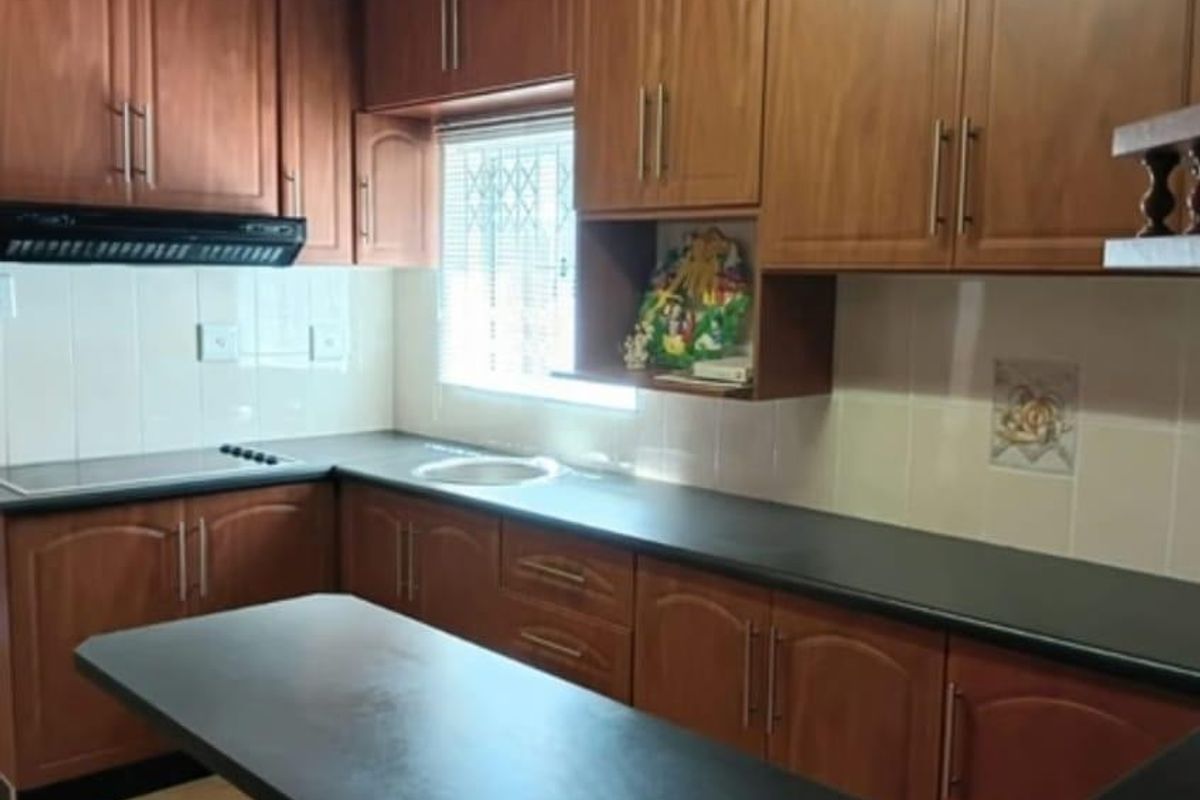 A functional kitchen featuring timber cabinetry, dark laminate countertops, a built-in extractor fan, and a timber-clad ceiling with tiled flooring.