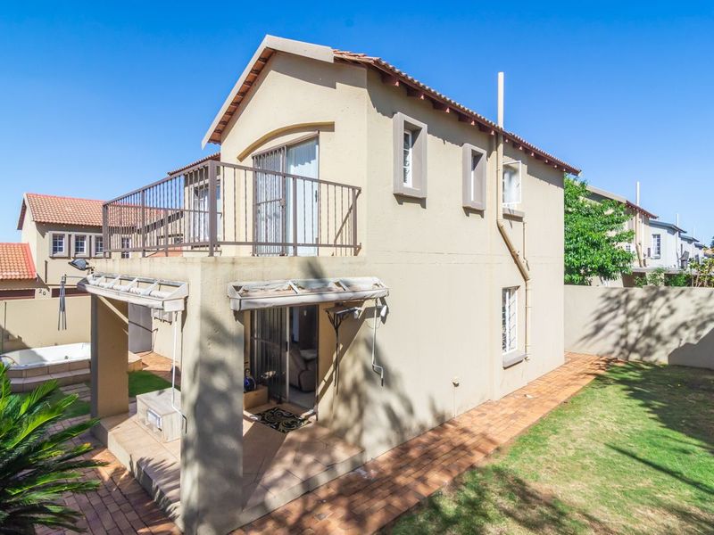 Rear view of a two-story townhouse featuring a covered patio, upper-level balcony, paved garden area, and a built-in spa.