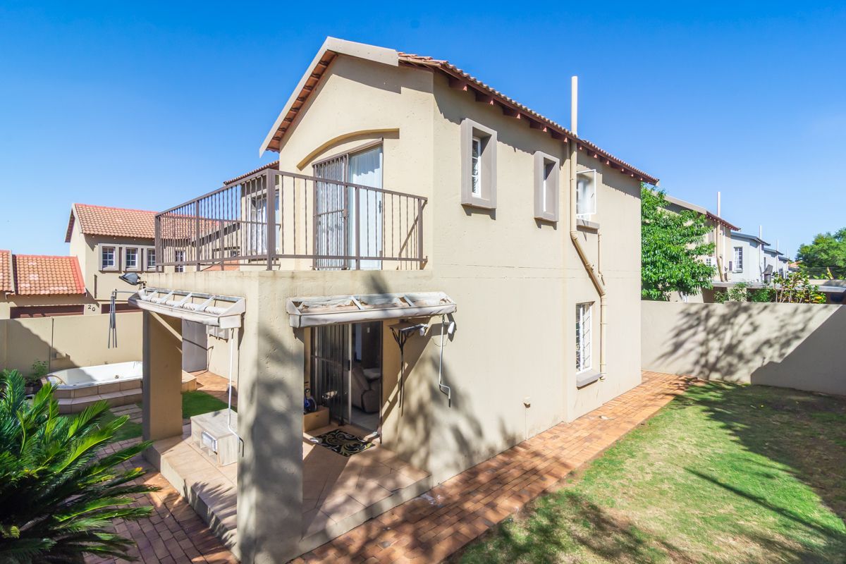 Rear view of a two-story townhouse featuring a covered patio, upper-level balcony, paved garden area, and a built-in spa.